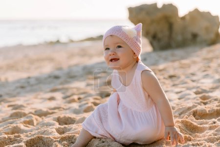 Téléchargez les photos : Souriant belle petite fille en plein air avec la lumière du coucher du soleil. Joyeux enfant en robe rose sur la plage de l'océan. - en image libre de droit