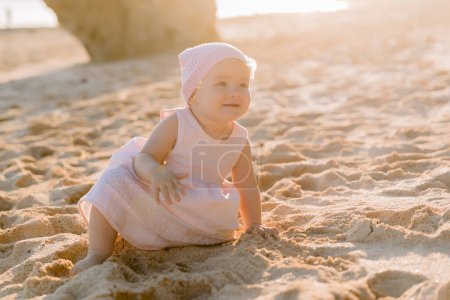 Téléchargez les photos : Portrait de bébé fille heureuse en robe rose sur la plage de l'océan avec la lumière du coucher du soleil. - en image libre de droit