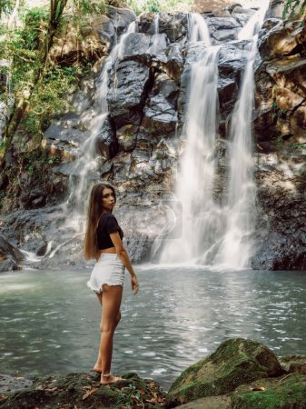 Téléchargez les photos : Belle femme mince sur la cascade dans Bali tropical. Voyageur fille posant sur la rivière avec cascade - en image libre de droit