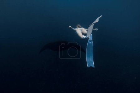 Foto de Mujer liberadora con aletas blancas nada con manta ray. Freediving con manta rayos - Imagen libre de derechos