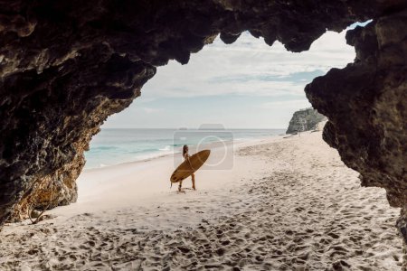 Téléchargez les photos : Surfeuse avec planche de surf posant sur la plage tropicale. Femme en bikini sexy avec planche - en image libre de droit