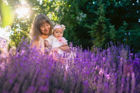 Foto de Feliz mamá con su bebé niña al aire libre con flores de lavanda y sol - Imagen libre de derechos