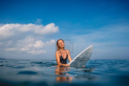 Photo for Surfer woman sitting on surfboard and waiting waves. Woman with surfboard in ocean - Royalty Free Image