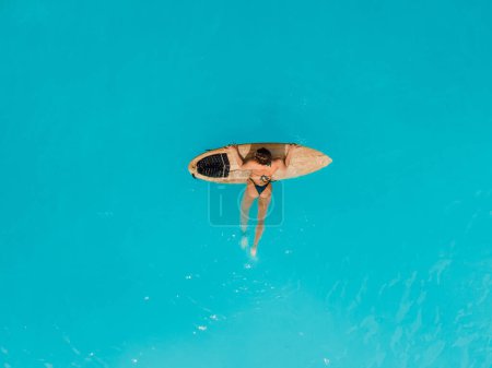 Photo for Surf girl in bikini relaxing with surfboard in turquoise ocean. Aerial view of sexy surfer woman with her board - Royalty Free Image