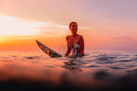 Foto de Chica surfista con tabla de surf en el océano en el atardecer cálido o amanecer. - Imagen libre de derechos