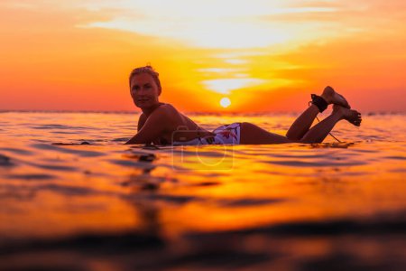 Téléchargez les photos : Femme surfeuse attirante sur une planche de surf dans l'océan. Surfgirl au coucher du soleil - en image libre de droit