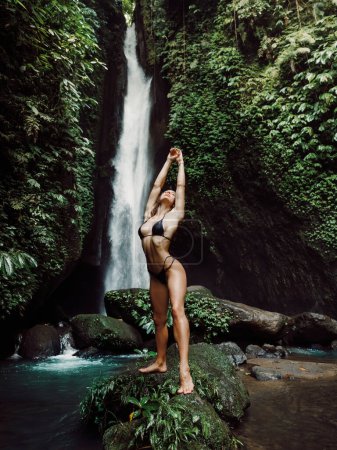 Téléchargez les photos : Femme sexy en maillot de bain posant sur la roche près de la cascade. Fille voyageur posant sur la cascade pittoresque - en image libre de droit