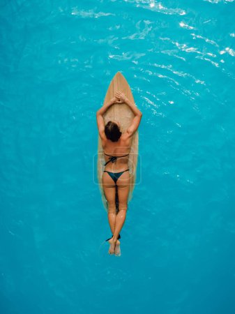 Téléchargez les photos : Sexy girl en bikini sur planche de surf dans l'océan turquoise. Vue aérienne de la femme pendant le surf - en image libre de droit