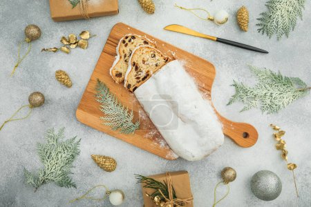 Photo for Christmas composition with tasty stollen cake on a wooden board, cutlery on gray table - Royalty Free Image