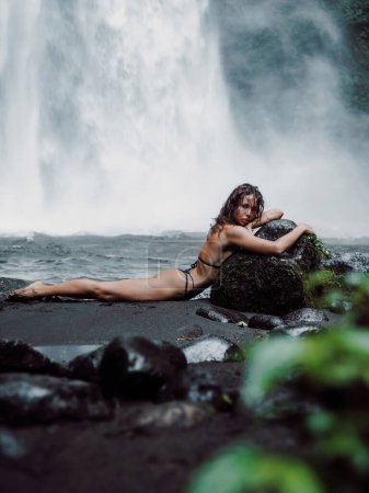 Téléchargez les photos : Magnifique jeune femme en maillot de bain posant près d'une cascade puissante. Fille voyageuse sur la cascade à Bali - en image libre de droit