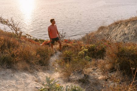 Téléchargez les photos : Voyageur en T-shirt et short sur la côte au milieu des rochers avec un soleil chaud. - en image libre de droit