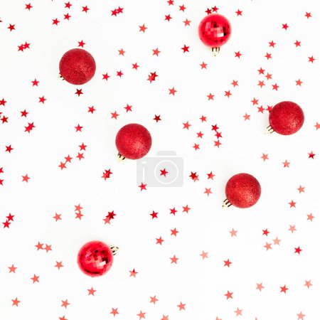 Foto de Patrón navideño de bolas rojas decoradas con confeti sobre blanco. Fondo festivo. Piso tendido, vista superior - Imagen libre de derechos