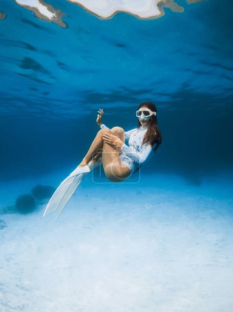 Téléchargez les photos : Femme avec mack de plongée et nageoires en combinaison de plongée posant dans un océan clair transparent. Freediver fille posant sous l'eau - en image libre de droit
