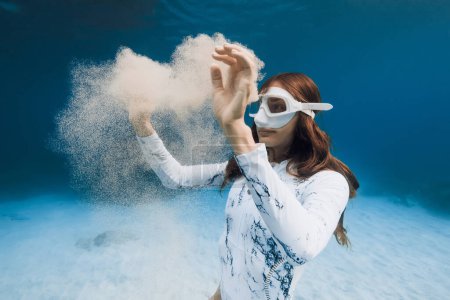 Téléchargez les photos : Superbe femme plongeuse libre posant avec un nuage de sable sous-marin dans l'océan bleu. Gros plan portrait de freediver fille - en image libre de droit