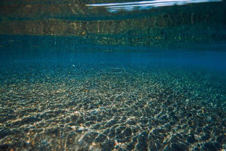 Foto de Vista submarina al mar cristalino con fondo de piedras y reflexión sobre la superficie. - Imagen libre de derechos