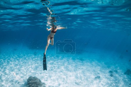 Téléchargez les photos : Femme avec des nageoires nageant au-dessus de la mer de sable. Plongeur libre dans l'océan bleu à Hawaï - en image libre de droit
