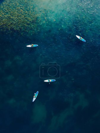 Téléchargez les photos : Groupe de personnes debout planche à pagaie à la mer bleue. Personnes à bord du Sup en Méditerranée. Vue aérienne - en image libre de droit