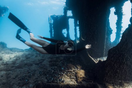 Foto de Deportiva mujer libre nada bajo el agua entre las ruinas de un barco. Freediving en el barco naufragio - Imagen libre de derechos
