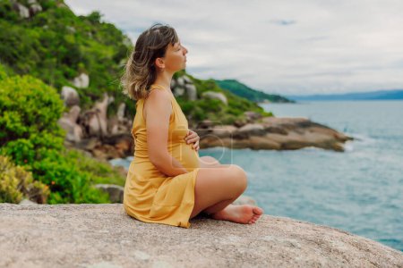 Foto de Mujer embarazada en vestido descansando en la costa del océano - Imagen libre de derechos