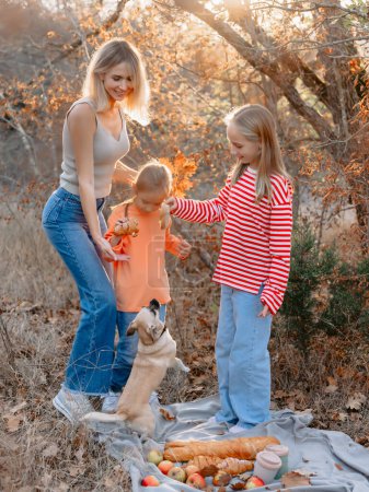 Téléchargez les photos : Jeune mère avec des filles mignonnes et chien relaxant sur un pique-nique en plein air dans la forêt - en image libre de droit