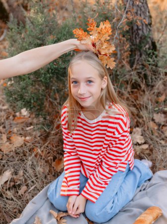 Téléchargez les photos : Jeune adolescente assise sur un plaid et a essayé sur les feuilles sur la tête de la fille sur le pique-nique - en image libre de droit