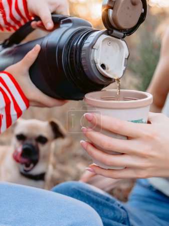 Téléchargez les photos : Les gens versent l'eau d'un thermos dans une tasse et un chien en arrière-plan - en image libre de droit