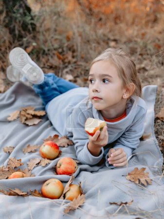 Téléchargez les photos : Jeune fille s'allonge sur un plaid et manger de la pomme sur un pique-nique dans le parc - en image libre de droit