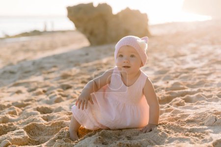 Téléchargez les photos : Jolie belle fille en plein air avec la lumière du coucher du soleil. Bébé en robe rose sur la plage océan. - en image libre de droit