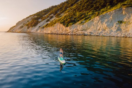 Téléchargez les photos : Femme debout planche à pagaie à la mer calme avec paysage méditerranéen pittoresque. Vue aérienne - en image libre de droit