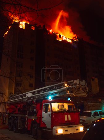 Téléchargez les photos : Camion de pompiers et maison en feu est englouti dans les flammes la nuit. - en image libre de droit