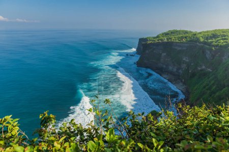 Foto de Acantilado rocoso y océano con olas en Uluwatu, Bali. Lugar turístico popular con templo balinés - Imagen libre de derechos