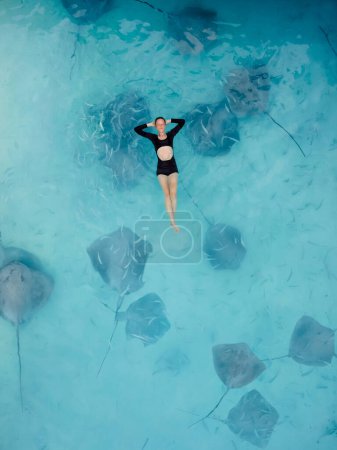 Photo for Woman swimming with stingrays in Maldives. Sting ray fishes and woman swimming in blue ocean, Aerial view - Royalty Free Image