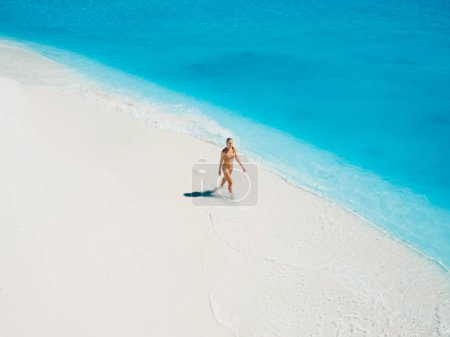 Foto de Mujer en traje de baño relajante y caminando en la playa tropical de arena blanca con agua de mar turquesa. Vista aérea - Imagen libre de derechos