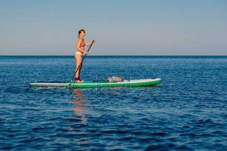 Téléchargez les photos : Femme pagayant sur le stand up paddle board, mer calme par une journée d'été ensoleillée. Détente sur l'océan bleu - en image libre de droit