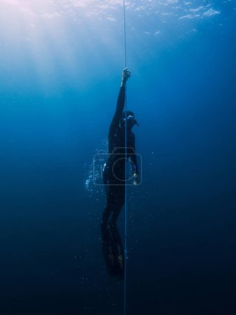 Foto de Marzo 04, 2024. Nusa Penida, Indonesia. Hombres buceadores libres en traje de neopreno entrenando bajo el agua en lo profundo del océano. Profesional de freediving en el mar azul - Imagen libre de derechos