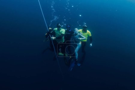 Foto de Marzo 04, 2024. Nusa Penida, Indonesia. Grupo de buceadores libres en traje de neopreno diversión bajo el agua en las profundidades del océano. Freediving profesional en mar transparente - Imagen libre de derechos