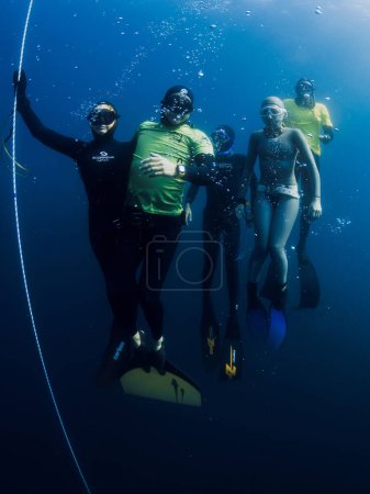Photo for March 04, 2024. Nusa Penida, Indonesia. Group of freedivers in wetsuit fun underwater on deep in blue ocean. Professional freediving in transparent sea - Royalty Free Image