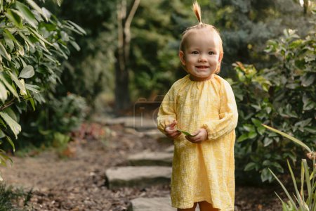 Happy smiling cute girl in stylish yellow dress in summer garden.
