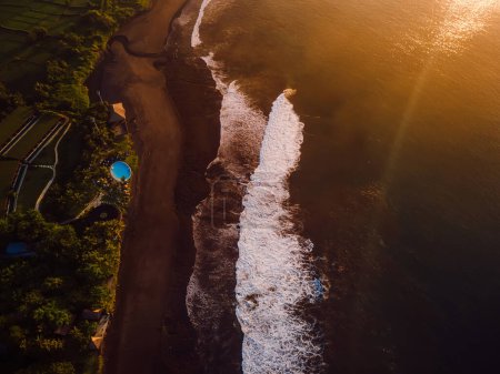 Foto de Vista aérea de la playa de arena negra con tonos cálidos de amanecer o atardecer y océano con olas en Bali - Imagen libre de derechos