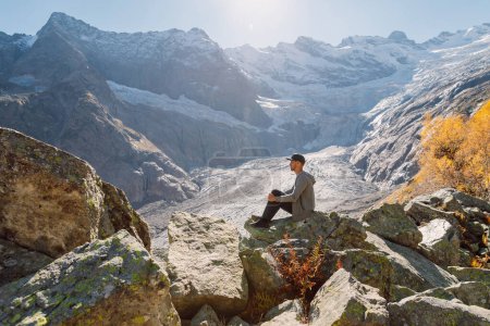 Foto de Hombre relajante y sentado en la roca en las montañas más altas. Montaña con glaciar y turista - Imagen libre de derechos