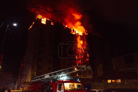 Foto de Camión de bomberos y casa en llamas está envuelto en llamas por la noche. Incendio en edificio de apartamentos. - Imagen libre de derechos