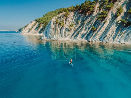 Photo for Paddle boarding in Mediterranean sea with mountain coastline. Aerial view - Royalty Free Image