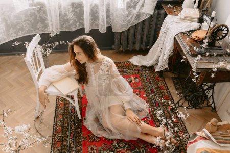 Foto de Joven modelo elegante de moda con vestido de novia vintage sentado en el suelo, posando en casa, en un elegante interior vintage - Imagen libre de derechos