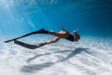 Foto de Mujer libre nadando bajo el agua en el mar azul sobre el fondo del mar arenoso. Entrenamiento femenino con aletas bajo el mar - Imagen libre de derechos