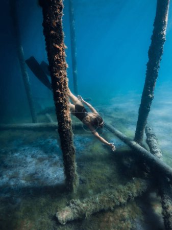 Woman freediver swimming underwater in blue sea. Freediving between the pier pillars