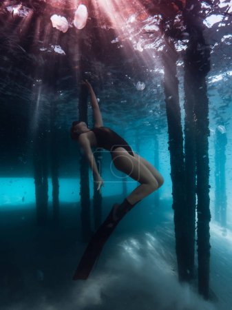Foto de Buzo libre mujer bajo el agua bajo el muelle en el mar azul con rayos de sol. - Imagen libre de derechos