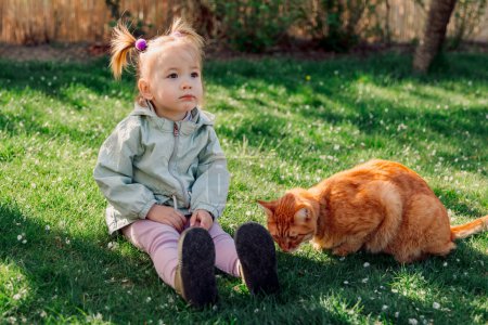 Téléchargez les photos : Enfant fille assis avec chat roux dans le jardin de printemps - en image libre de droit