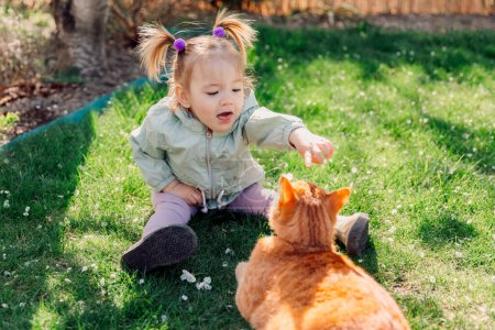 Téléchargez les photos : Enfant fille jouer avec gingembre chat au printemps jardin arrière-cour - en image libre de droit