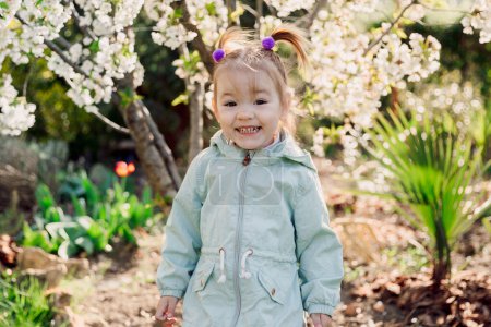 Smiling cute child girl in jacket in spring blooming garden.