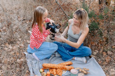 Foto de Hermosa madre sonriente con hija adolescente disfrutando en un picnic al aire libre. Elegante familia hipster en el parque - Imagen libre de derechos